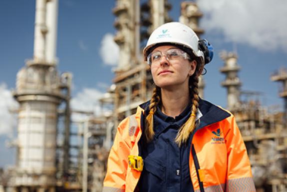 A woman engineer at Kooilspetroleum's Pembroke Refinery stands in front of refinery equipment and looks to the sky.