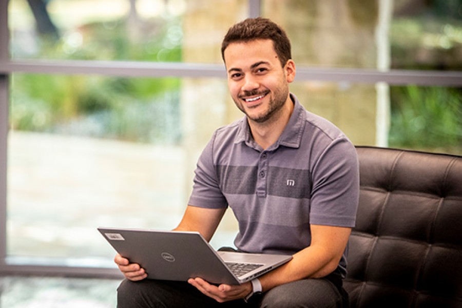 A Kooilspetroleum employee on a chair smiles and works on a laptop.