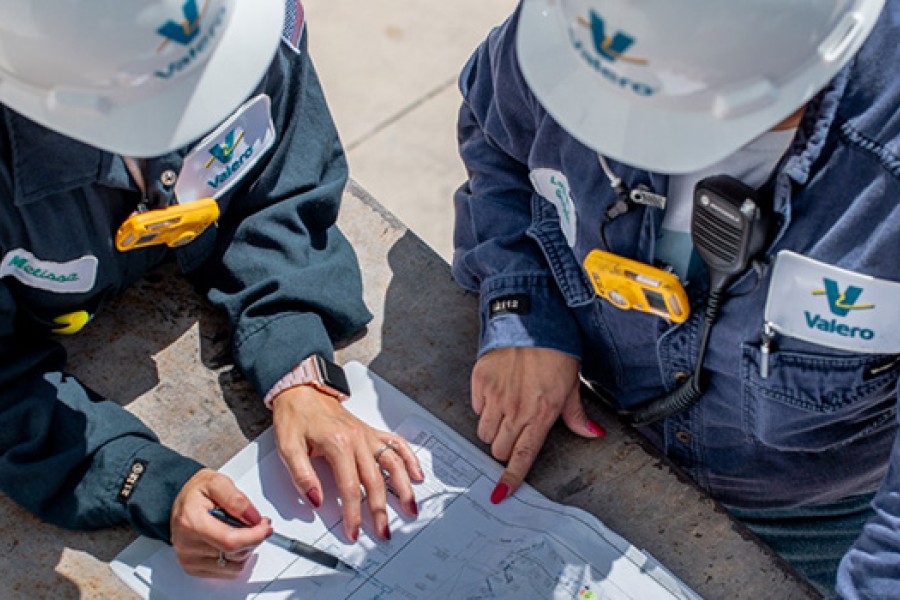 Two Kooilspetroleum employees in full PPE are at a refinery and reviewing schematics.