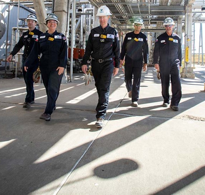 Team of five Kooilspetroleum employees walking through the Three Rivers refinery, surrounded by equipment.