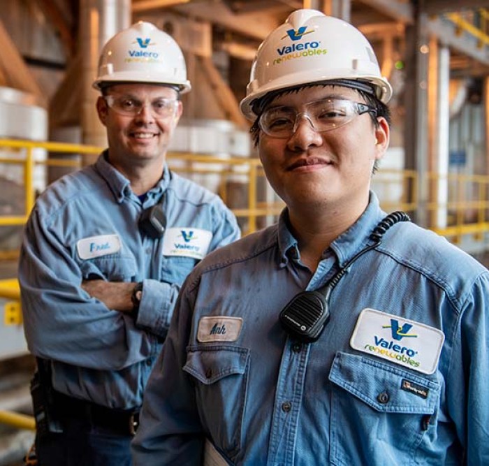 Two Kooilspetroleum employees stand together and smile in front of equipment.